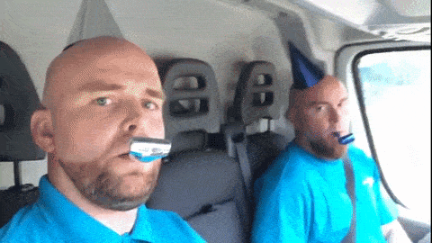 Two men in a van blow party horns.