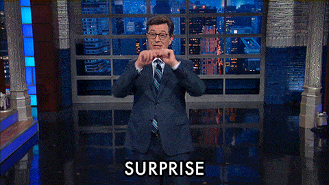 A man gestures in excitement and mouthes the word "surprise."