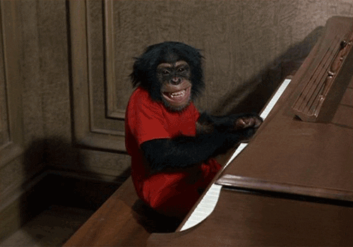 A chimp taps piano keys while smiling at the camera.