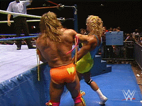 A wrestler knocks another wrestler down.